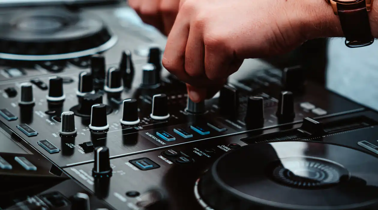 Close-up of hands adjusting controls on a DJ mixer, surrounded by various knobs and buttons.