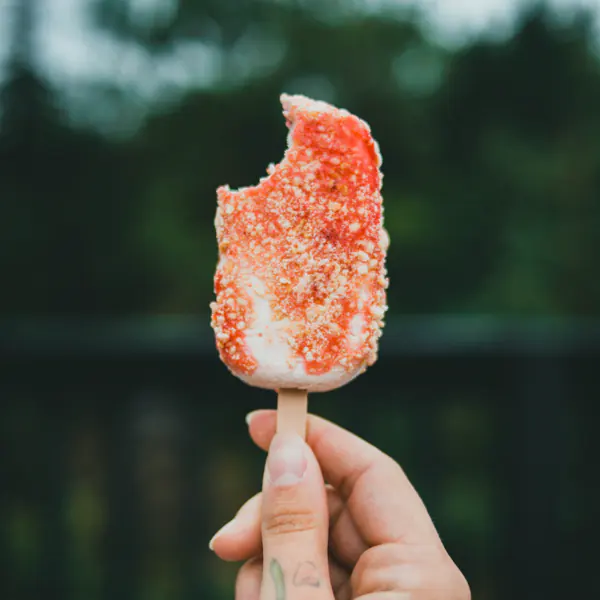 A hand holds a partially eaten ice cream bar coated with red and white sprinkles.