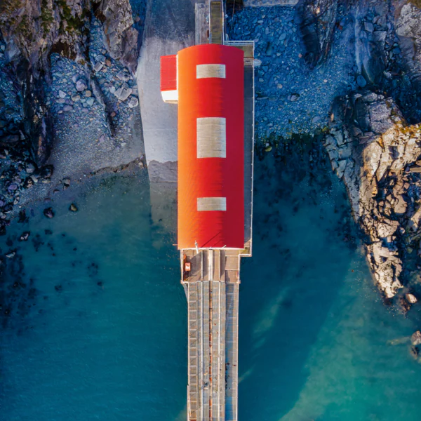 Aerial view of a red-roofed building on a dock extending over turquoise water, surrounded by rocky shoreline.