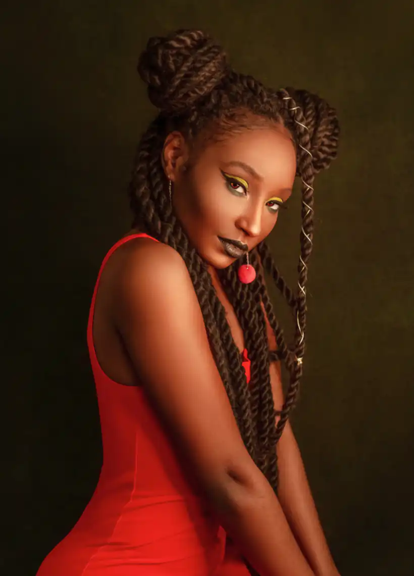 A woman with braided hair and two buns, wearing a red outfit, poses against a dark background.