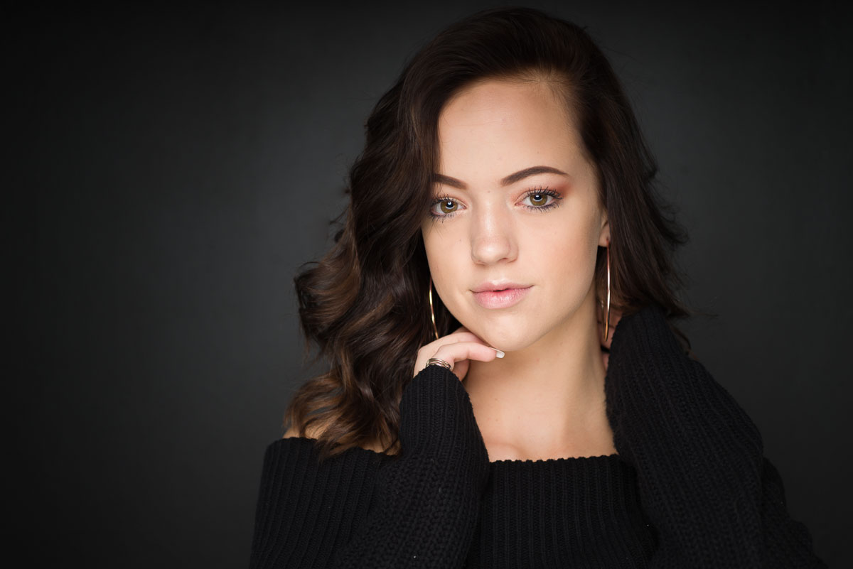 A young woman in a black sweater posing for a portrait at home.