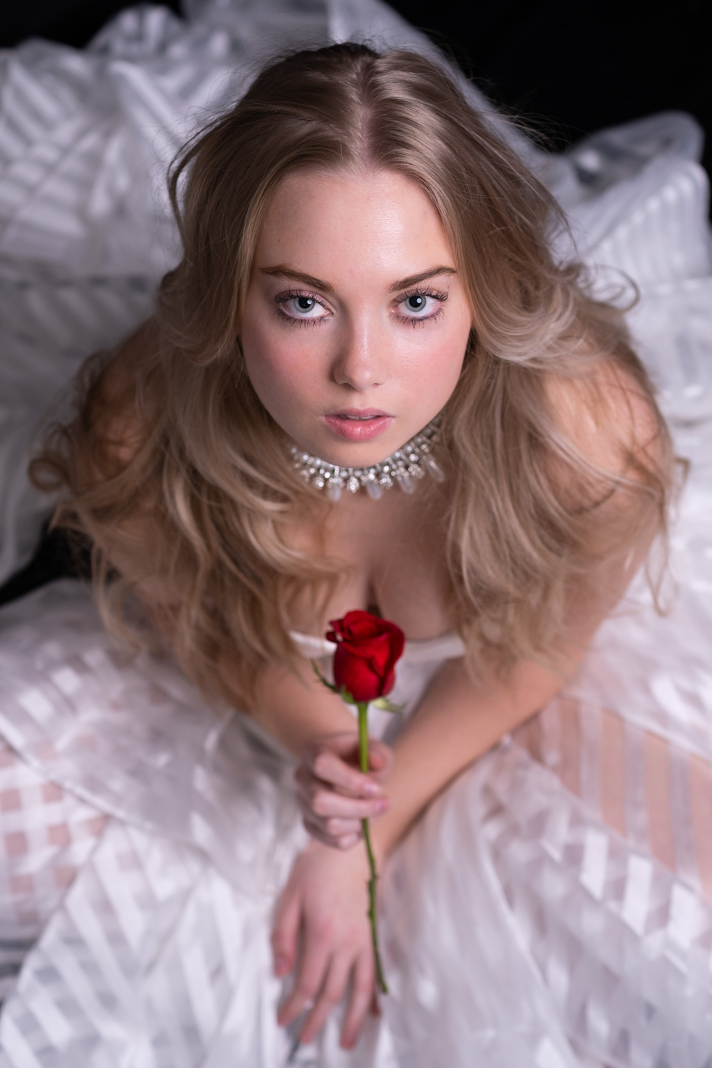 A beautiful woman in a white dress holding a red rose.