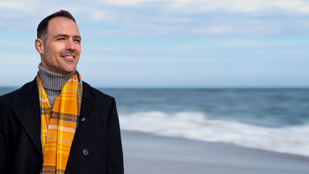 A man in a scarf posing for headshots on the beach.