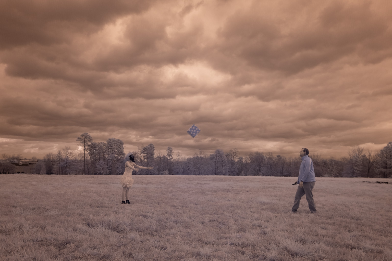 Two people celebrate a pandemic birthday by flying kites in a field under a cloudy sky.