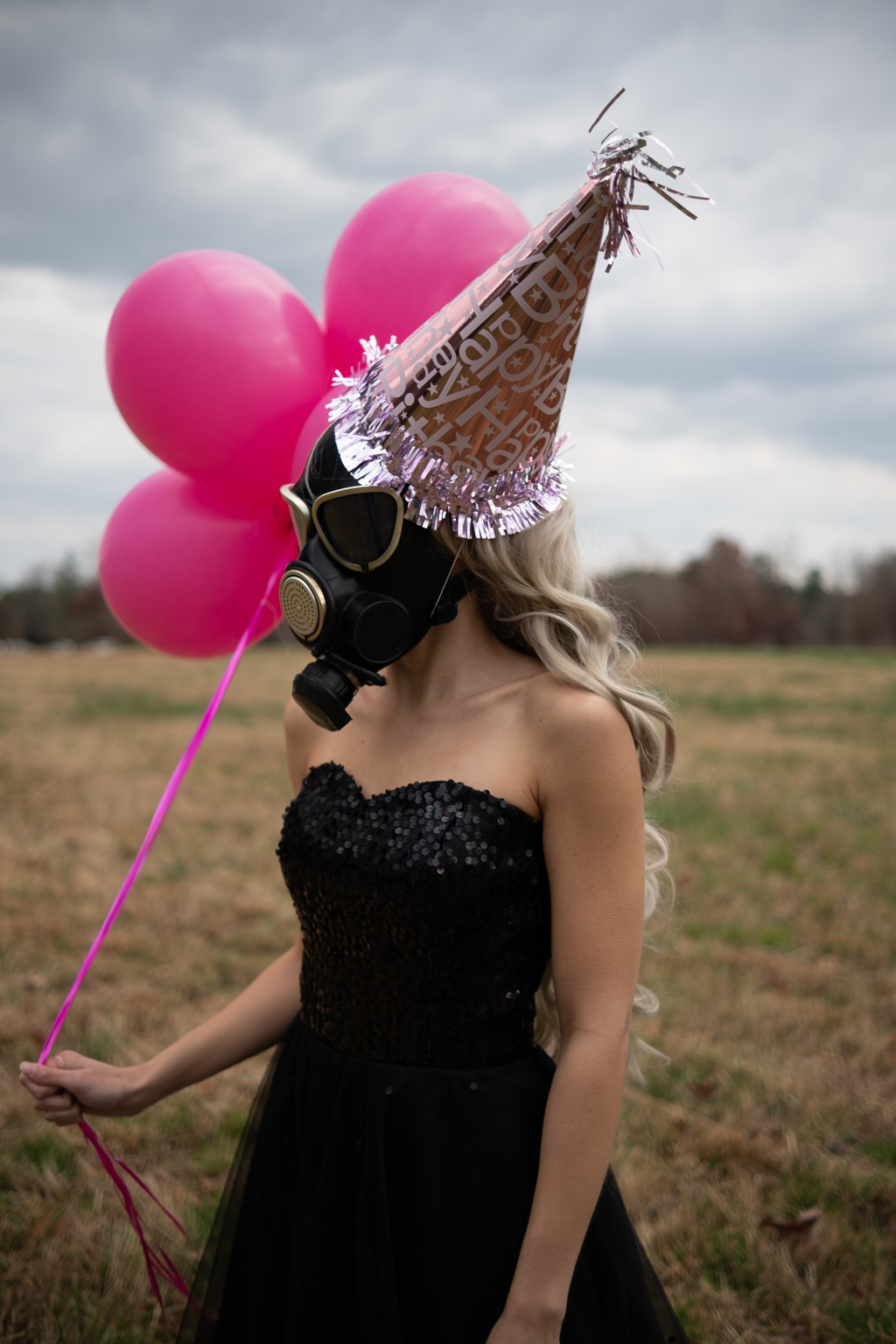 A woman celebrating her pandemic birthday dons a gas mask while holding pink balloons.