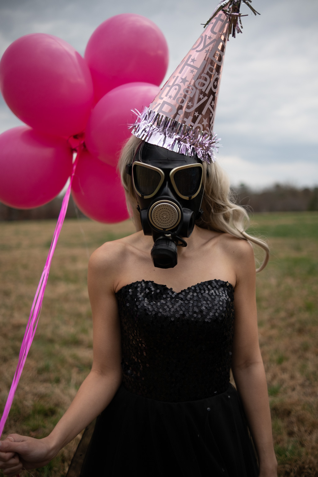 A woman donning a gas mask embraces pandemic-induced celebrations with pink balloons.