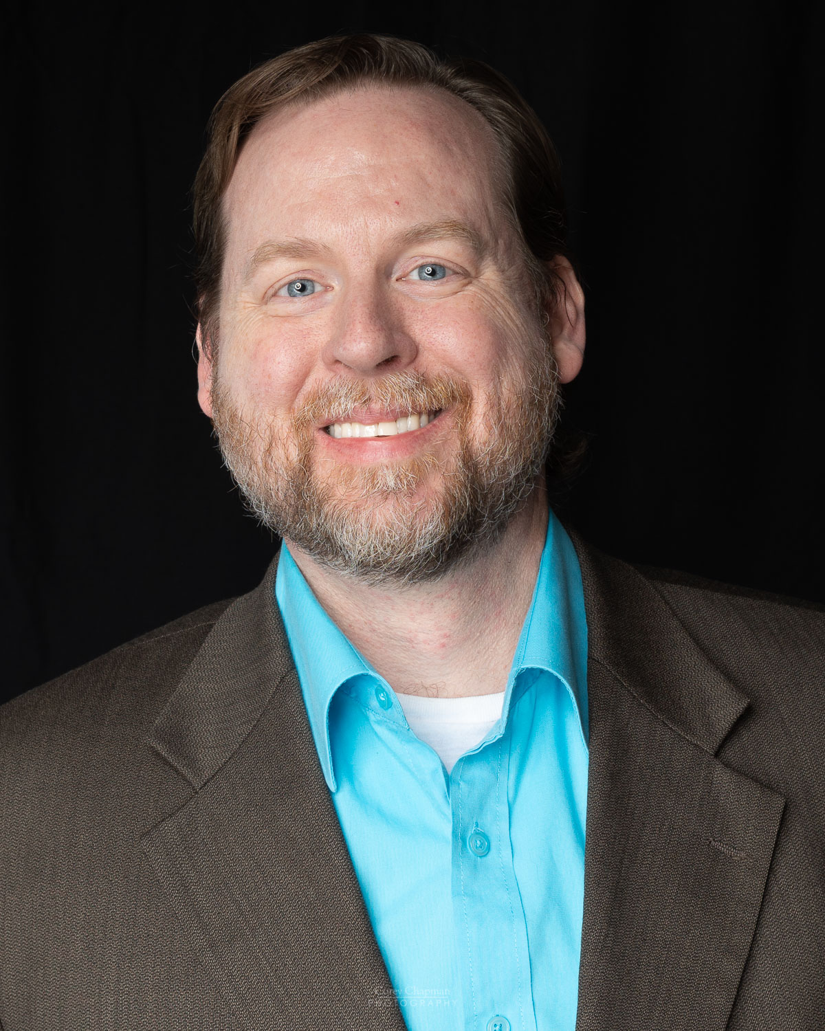 A man with a beard and a blue shirt ready for headshots in 2022.