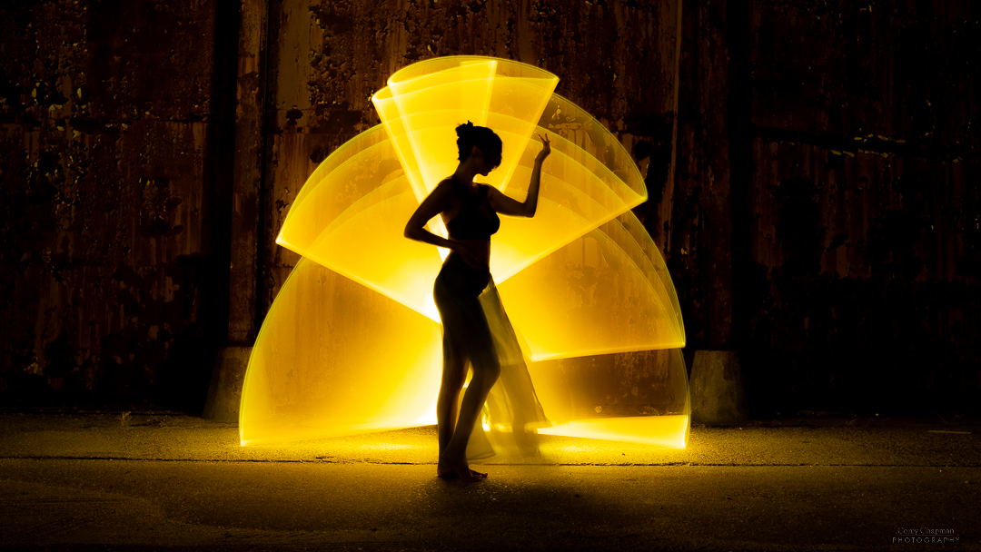 A woman standing in front of a sculpture illuminated by yellow light.