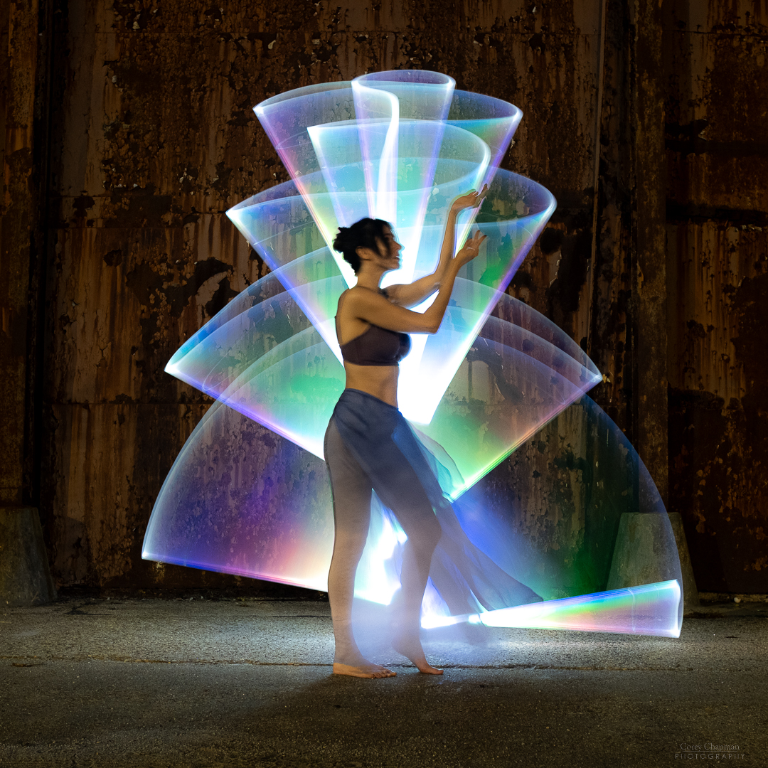 A woman is gracefully dancing in front of an intricate light sculpture.