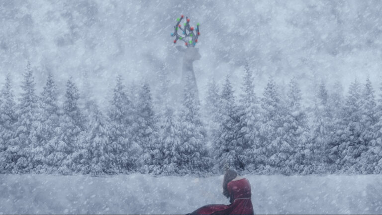 Person in red dress sits on snow in a forest during a snowstorm. A tall structure with colorful decorations is faintly visible in the background.