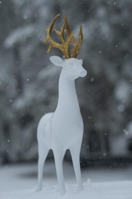 A white deer sculpture with golden antlers stands majestically in the snowy landscape, evoking a sense of Christmas magic.