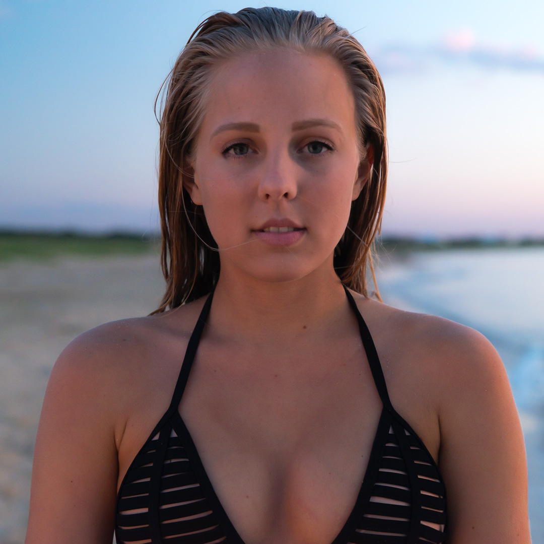 Person standing on a beach at sunset, wearing a black swimsuit.